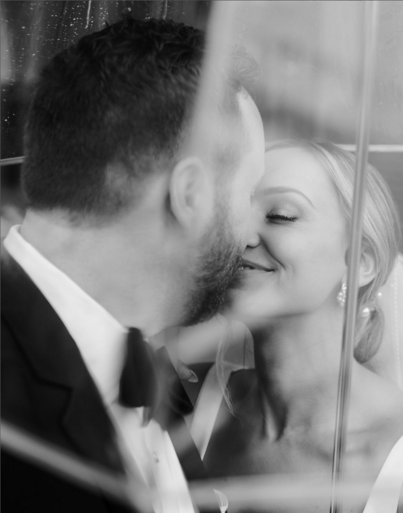Groom in tux kissing bride under an umbrella in Black and White.