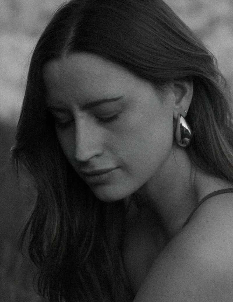 wedding photographer self portrait as the beautiful brunette woman is wearing an all white pant suit, gold rings and large pearl and gold vintage earrings.