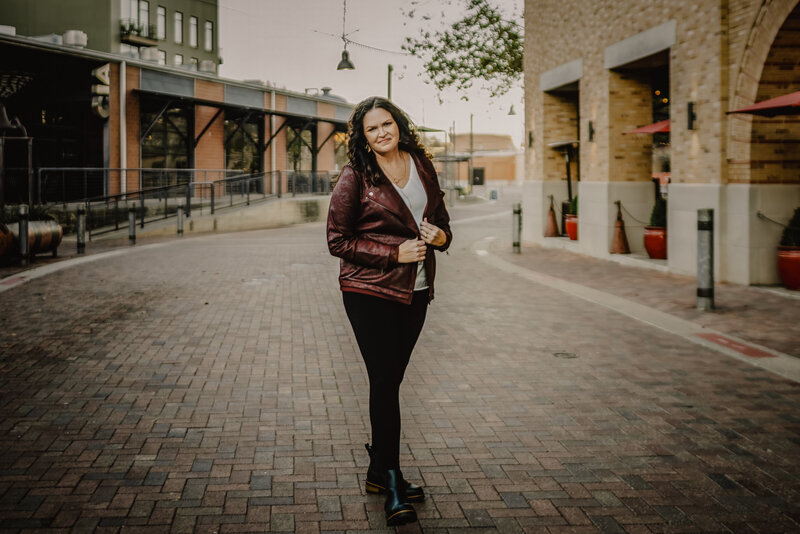 Photographer Jennifer in maroon jacket leaning toward camera during personal branding session in downtown San Antonio, Texas.