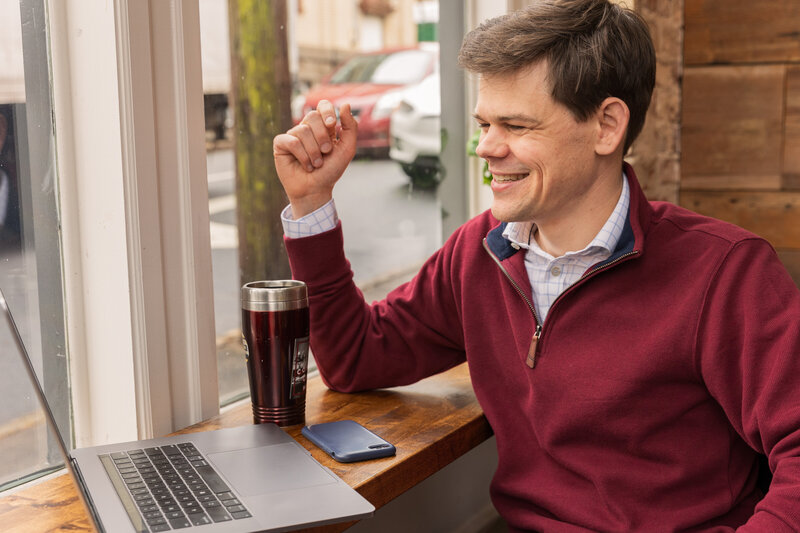 man sitting in a coffeeshop and having a zoom meeting on his laptop during personal brand photoshoot Atlanta Brand Photographer