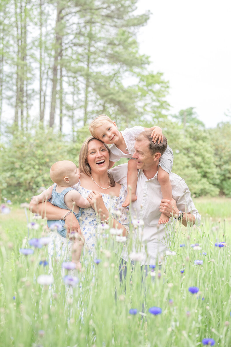 family smiling in a field taken by Apex Newborn Photographer