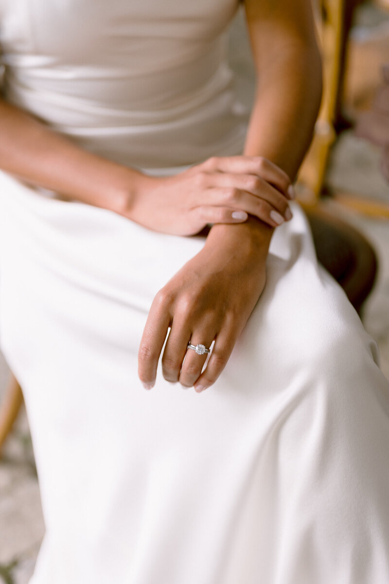 A person seated in an elegant white dress, showcasing a ring on their finger.