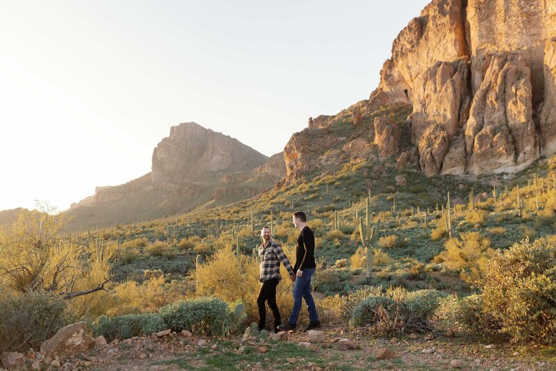 Couple walk through spacious desert for engagement photos.
