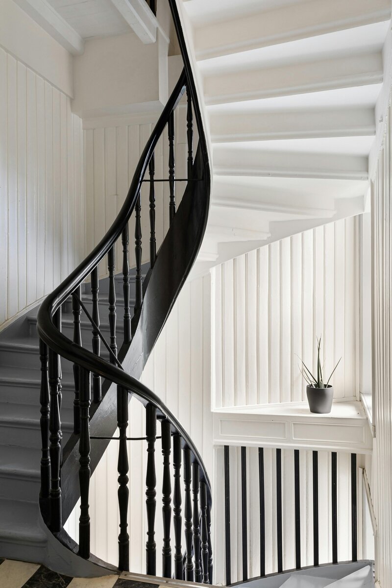 Historical home twisting staircase. White shiplap molding. white walls. black staircase. hand turned staircase spindles.