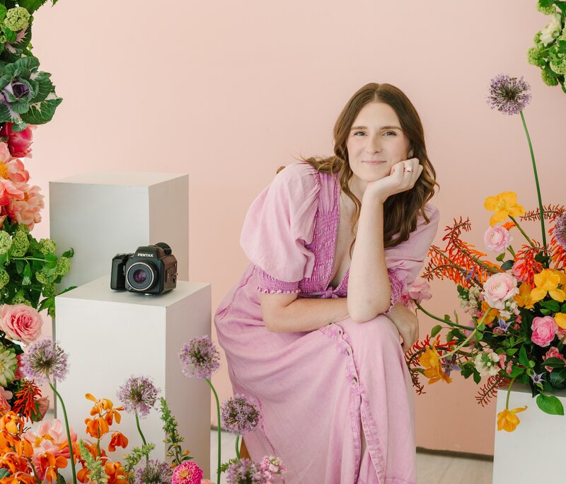 Headshot of Aly Matei sitting on a stool holding her camera