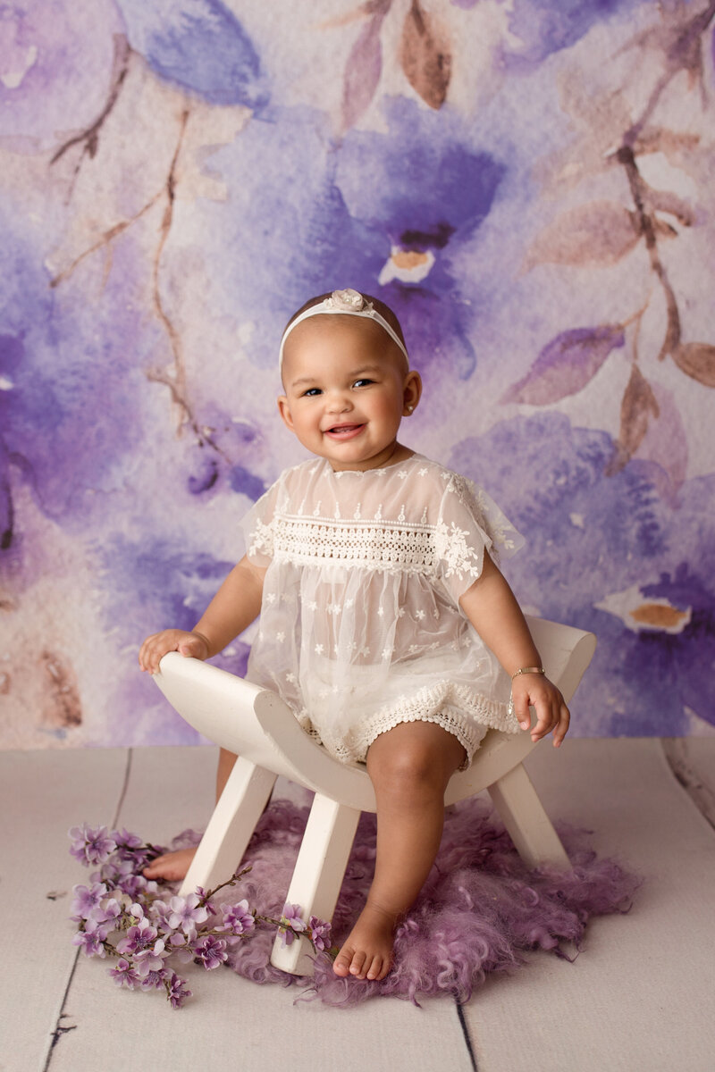 baby girl on a purple backdrop wearing lacy cream outfit