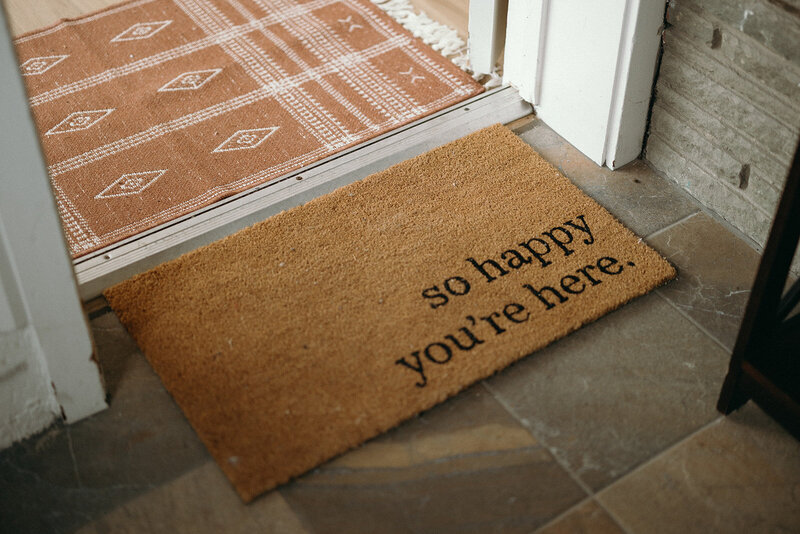 The welcome mat that says "so happy you're here" at the door of Janna's wellness center, The Eyrie Eagle's Guiding Light.
