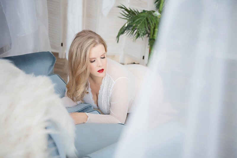 Stunning boudoir portrsit of blonde woman leaning over light blue suede couch