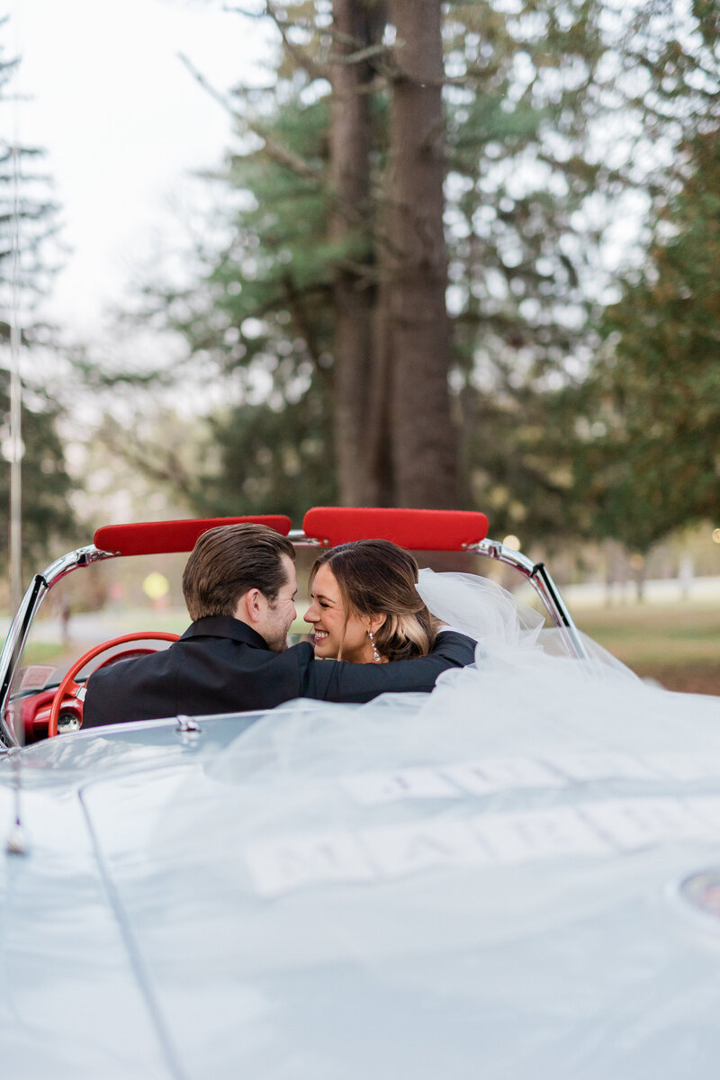 Newlyweds drive off smiling in a white convertible 