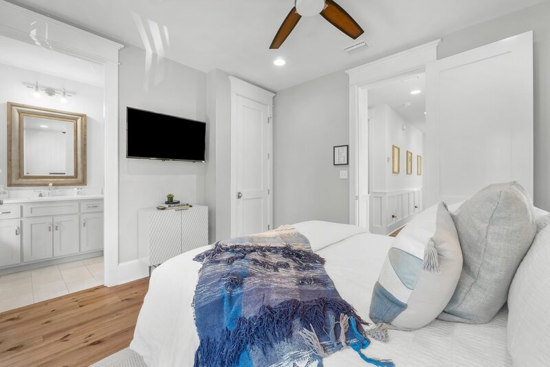 Serene queen bedroom with ensuite bath, smart TV, ceiling fan, and hallway access at luxury Panama City Beach retreat.