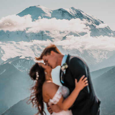 a couple embraces in front of the snowy Mount Rainier . Their blurred embrace frames the sharp mountain during their mount Rainier elopement