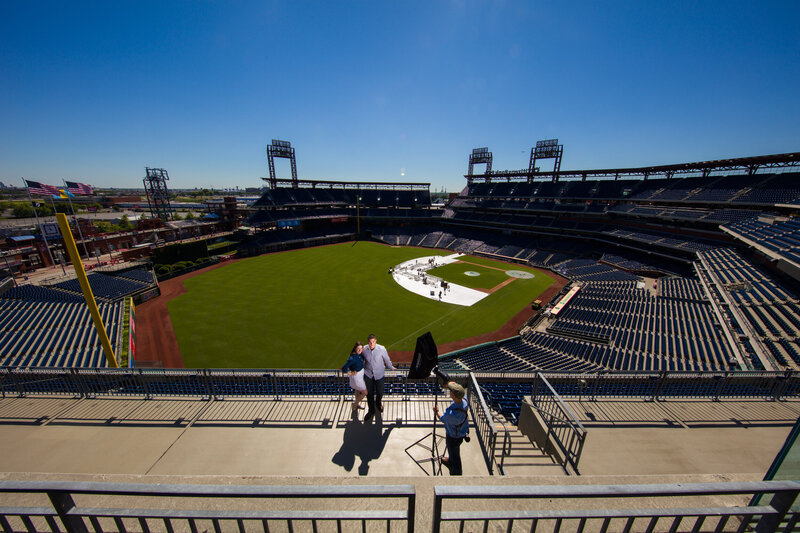 Travis Stitt setting up lighting for an engaged couple overlooking Citizens Bank Park, home of the Philadelphia Phillies MLB, during an engagement session, capturing a romantic and striking moment with the iconic ballpark as a backdrop.