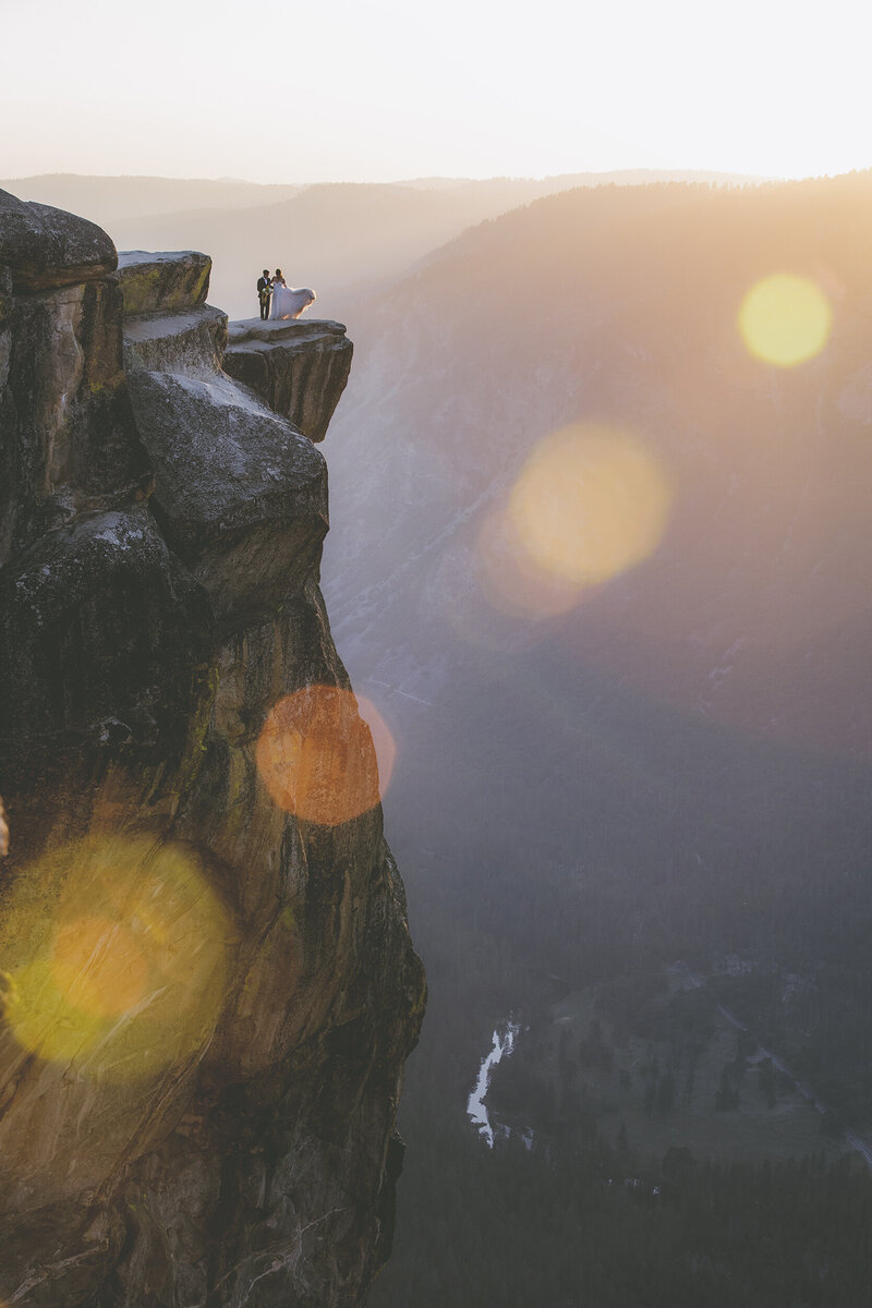 A telephoto shot of a bride and groom posing on a ledge at Taft Point in Yosemite during their adventure elopement.