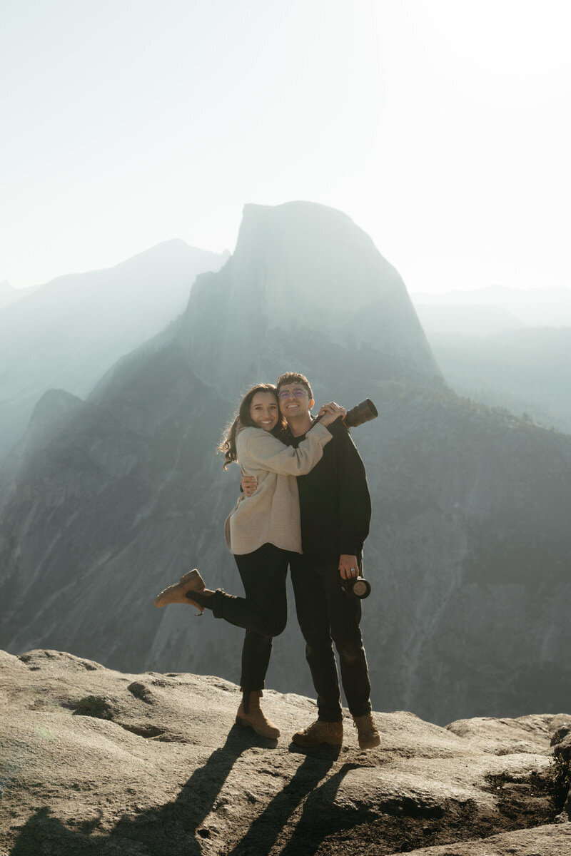 Glacier Point Elopement Photographers The Chaffins standing in front of Glacier point smiling with cameras in their hands