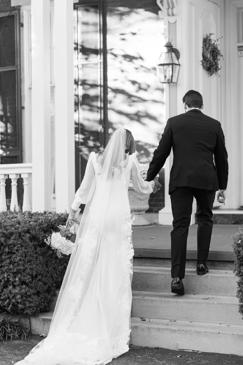 Black-and-white photo of a bride and groom walking up steps hand in hand.