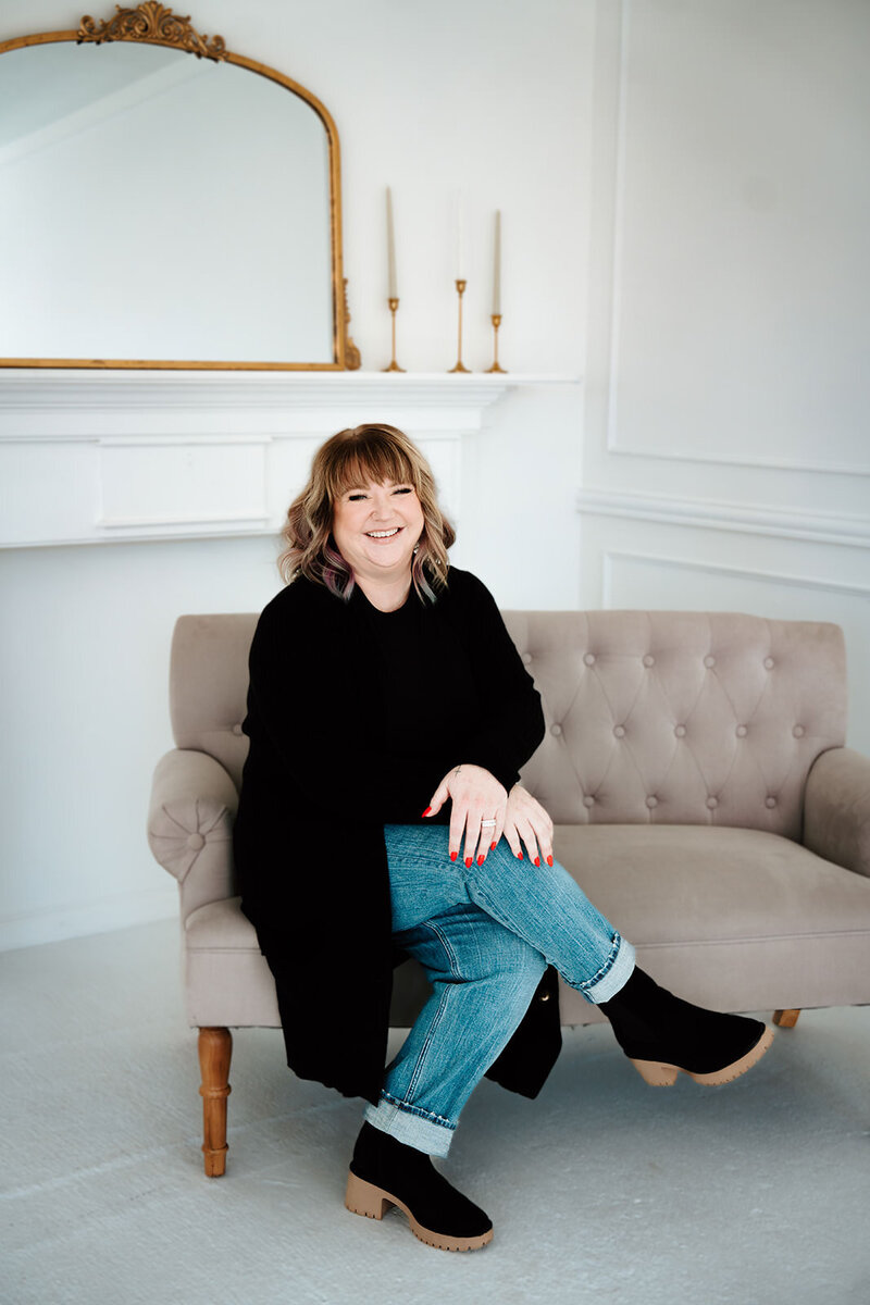 woman in green top sits on a leather couch and works on a notepad on a table