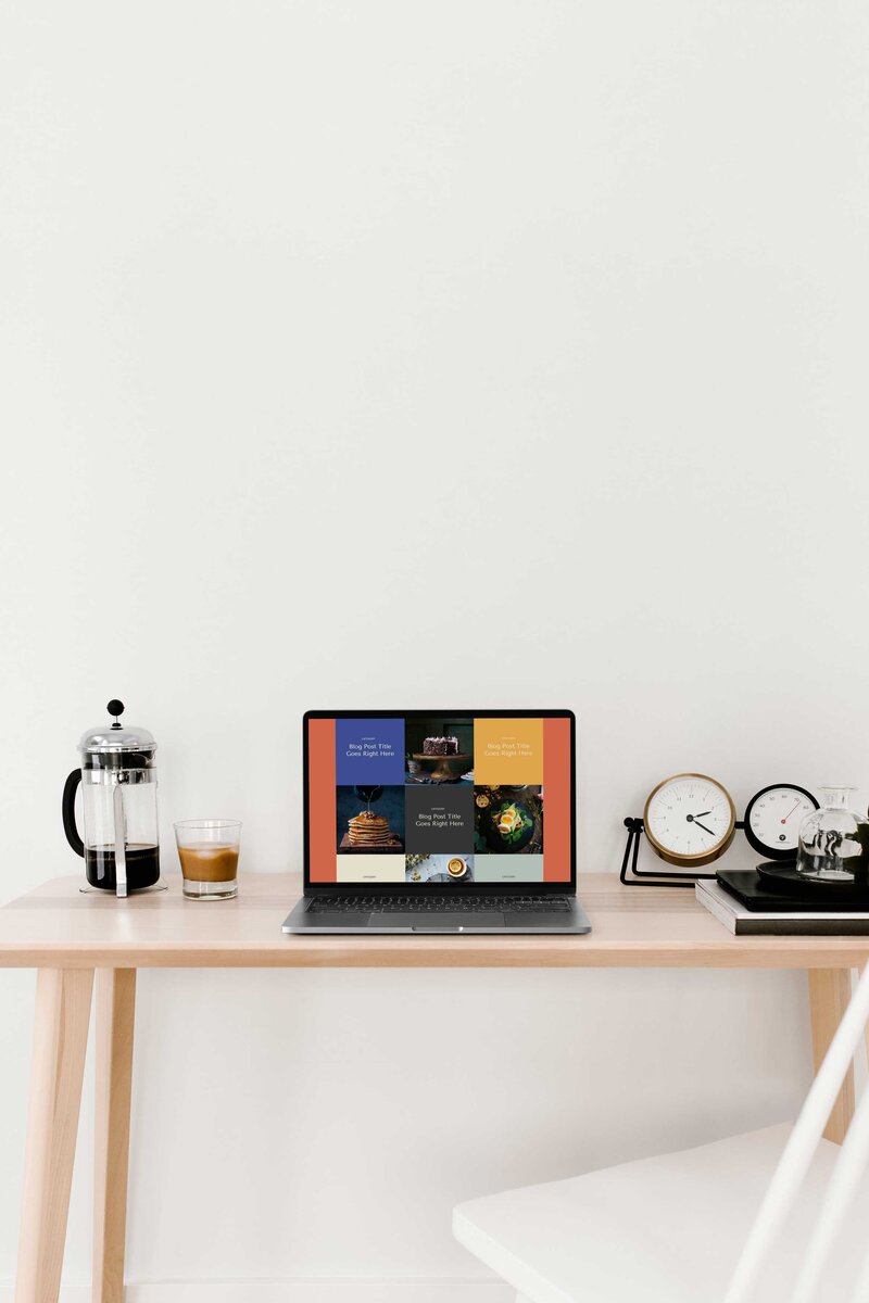 A laptop on a desk next to coffee and clocks.