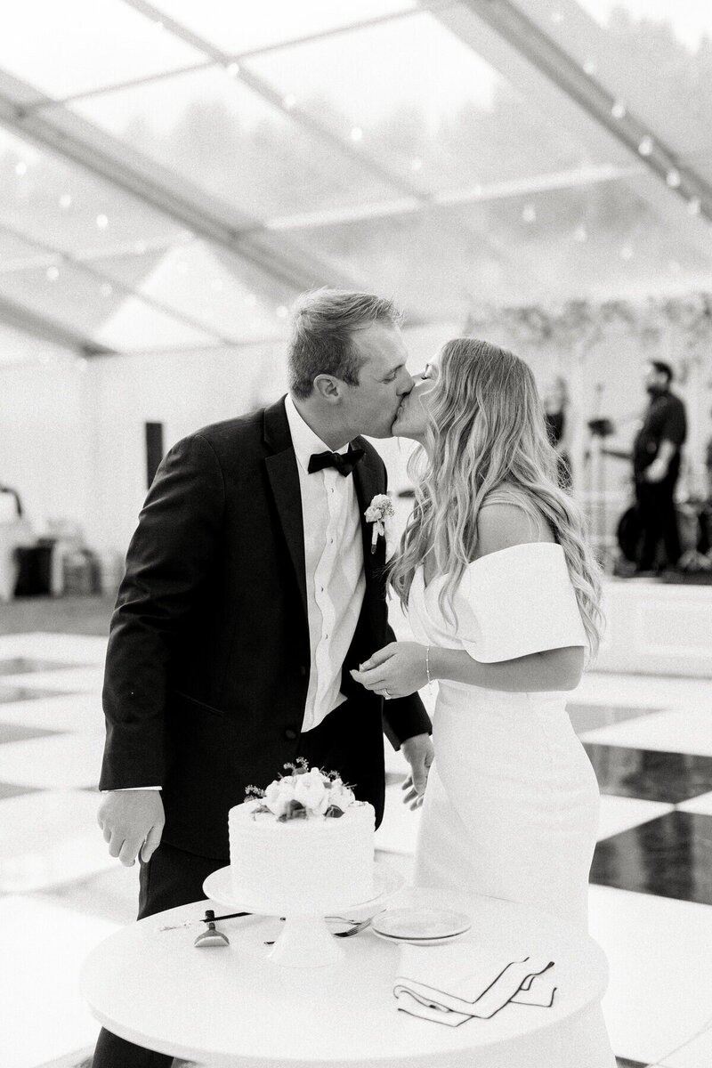 Happy wedding couple kissing while cutting their cake, beautifully photographed by a Milwaukee wedding photographer Emily Barbara.