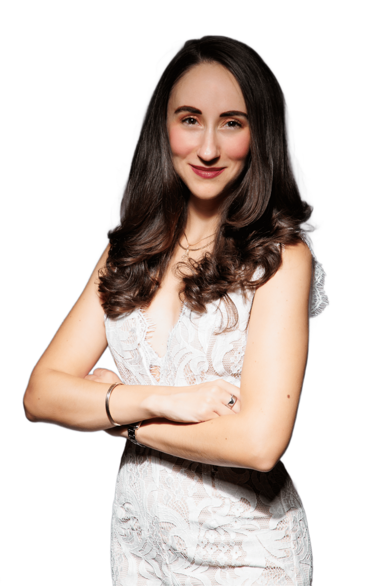 Corinne smiling confidently with arms crossed, wearing a white lace top