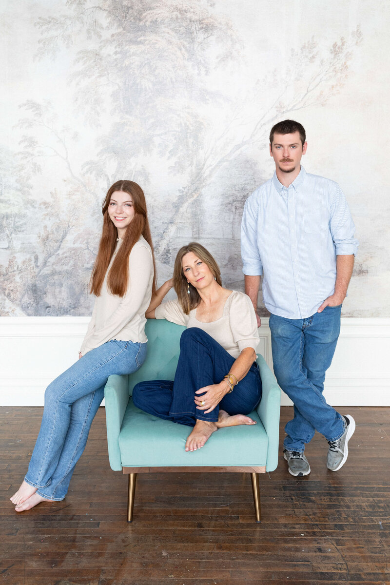 family of 3 wth brunette hair and red hair wearing blue jeans sitting in a studio