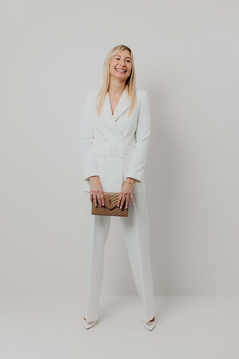 A blonde women in a white power suite holding a brown purse;
