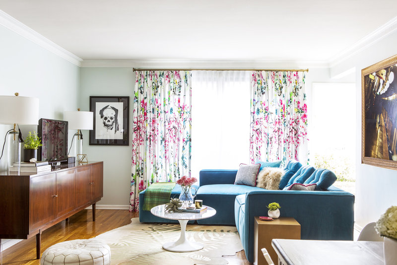 Living room with teal velvet sectional, metallic zebra rug, marble tulip coffee table, and  modern floral drapes