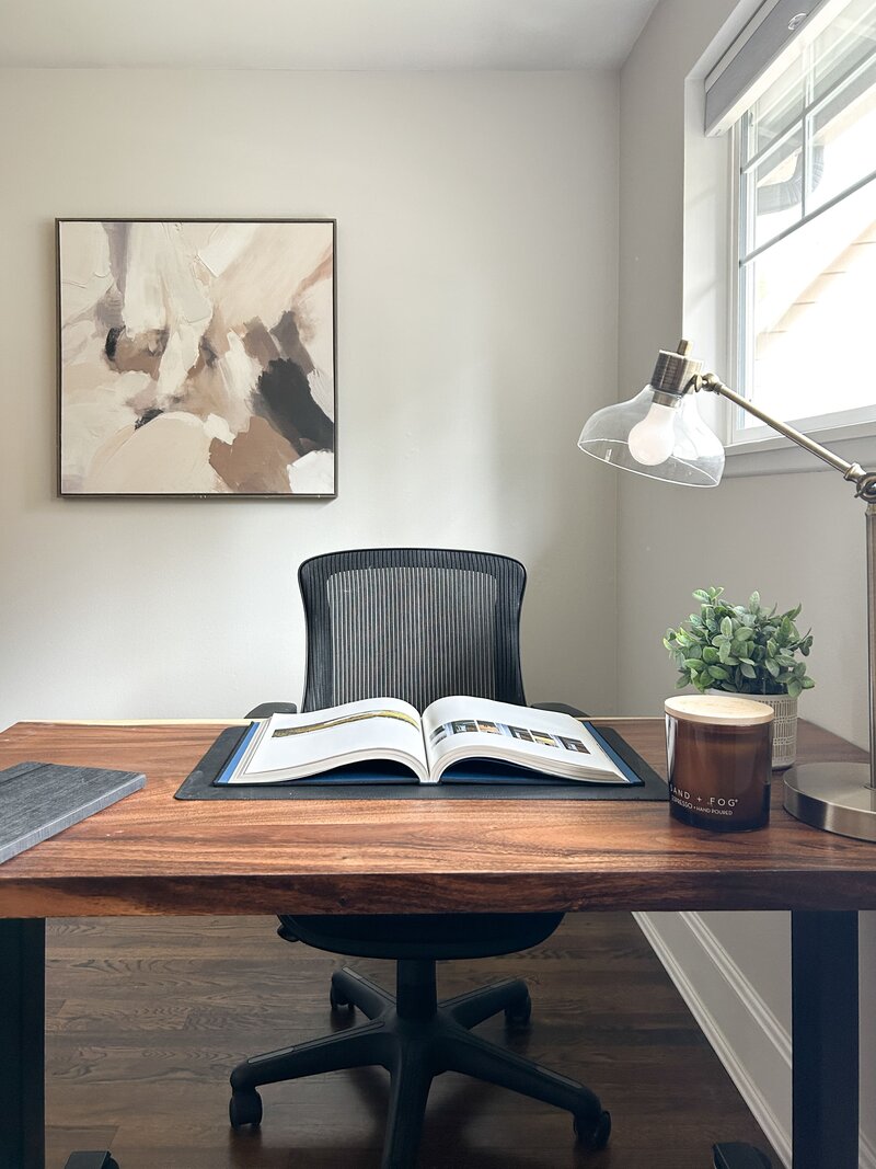 Modern home office staged by Modern Mollusk in Snohomish County featuring a wooden desk, open book, and neutral abstract art on the wall.