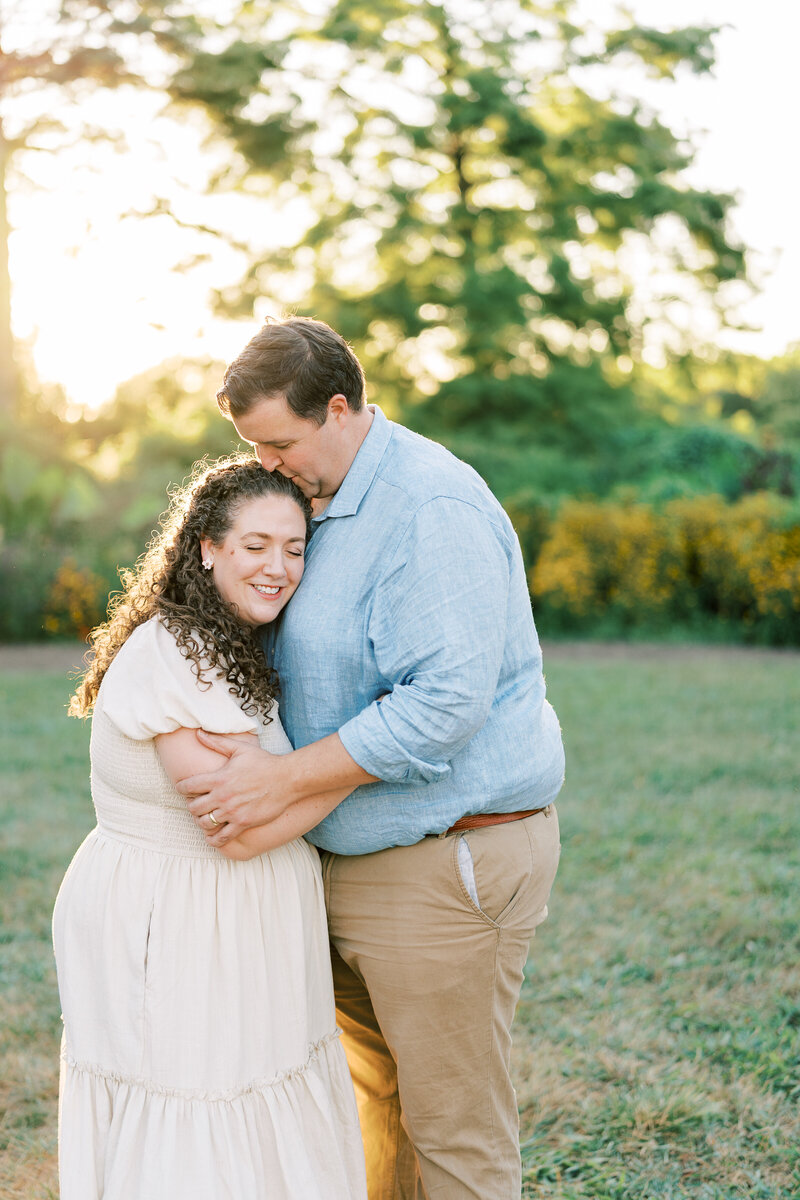 Fine art Catholic wedding photographers Laura and Matthew Schaefer with arms linked, standing under a tree, and smiling at the camera