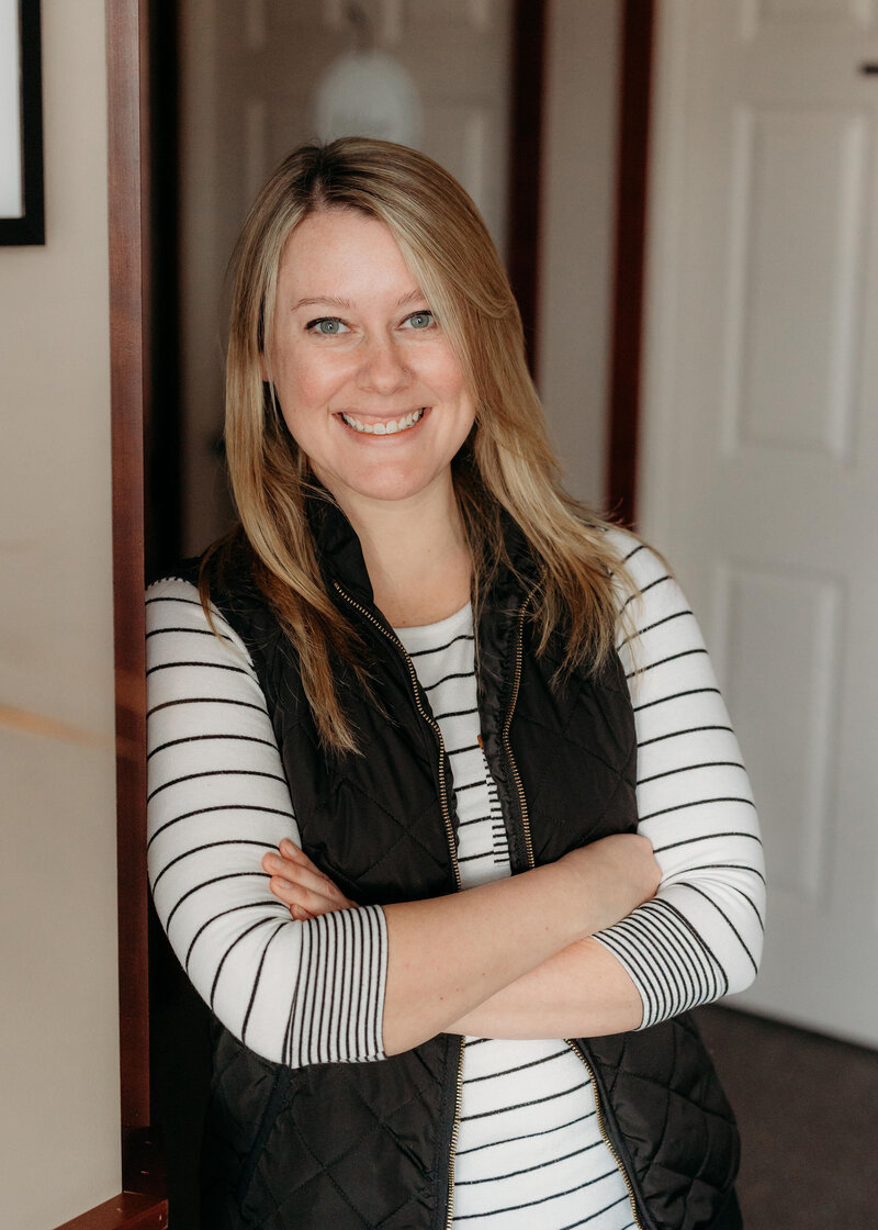 Chiropractor Brittany Fisk standing with arms crossed, smiling in hallway at Busy Bee Chiropractic clinic.