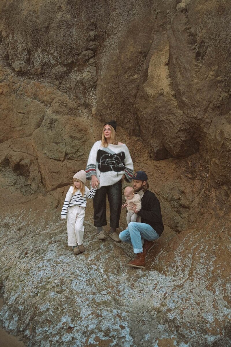 a stylish male and a female with daughter and baby standing on rock at beach