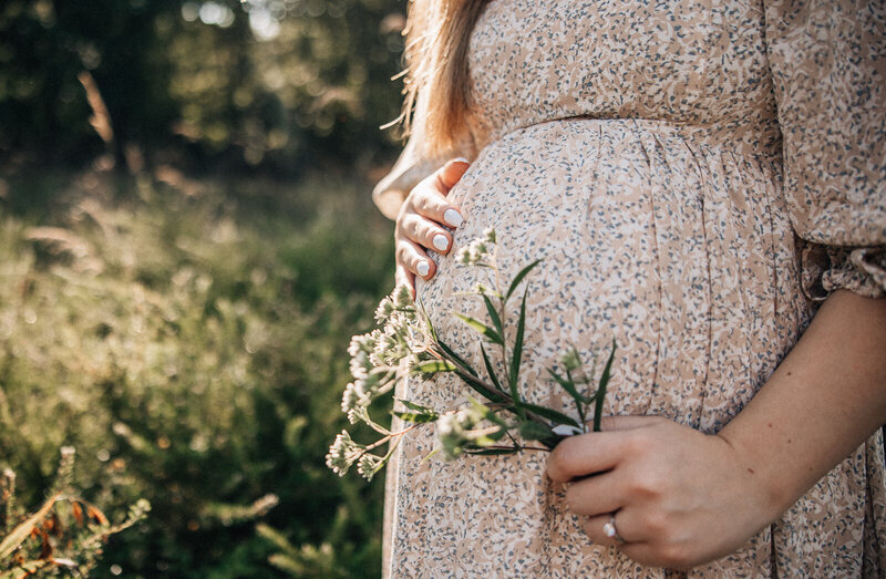 Maternity portrait of mom's belly in a floral dress and hands holding a flower at sunset. 