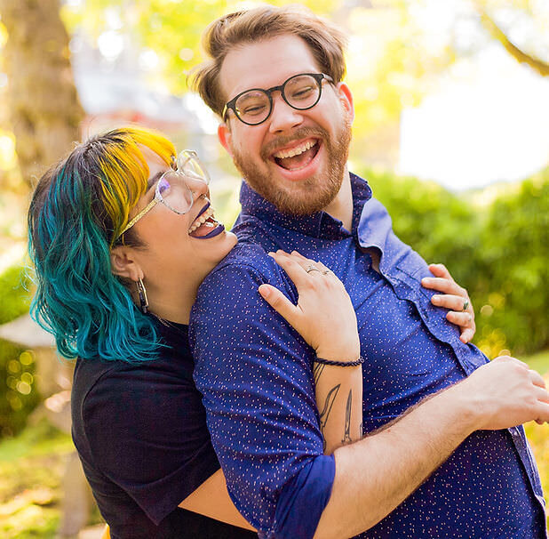 couple standing behind each other smiling as one holds the other from behind