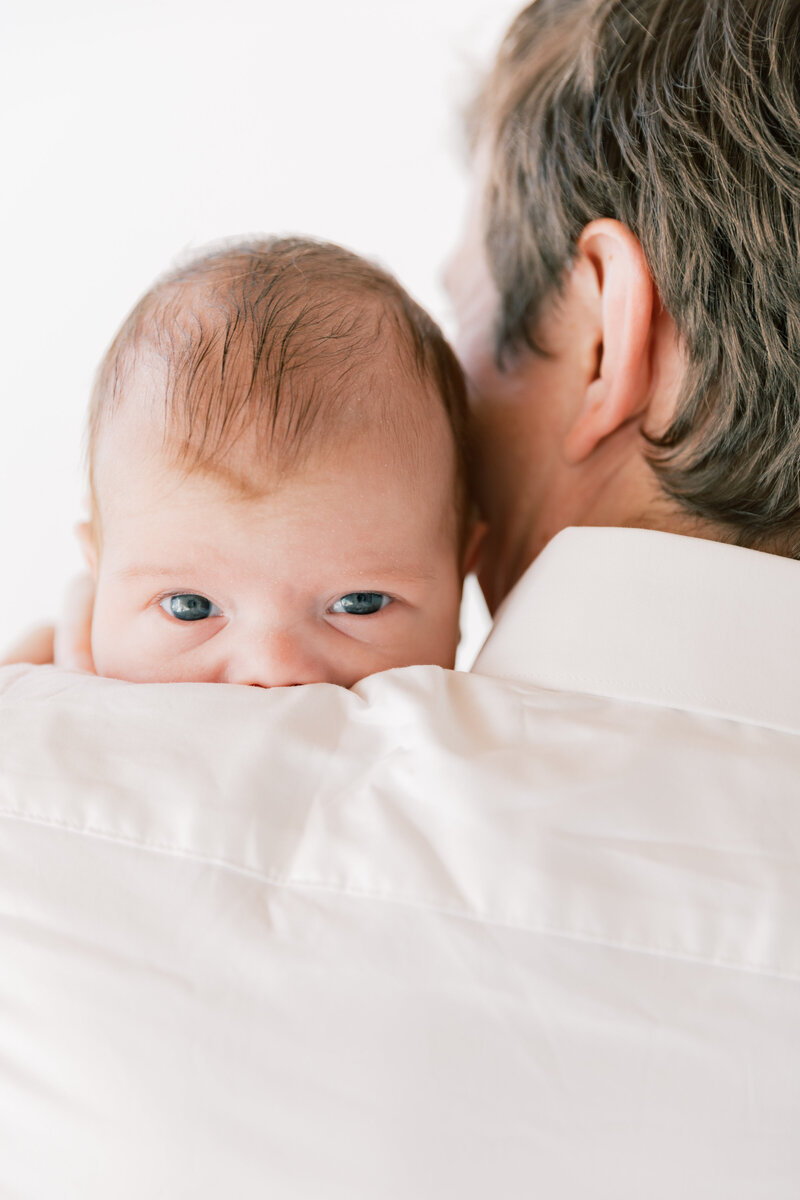 A newborn baby peeks over dad's shoulder