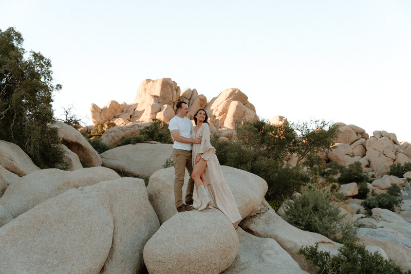 A couple standing on a boulder in Joshua Tree National Park celebrating their engagement.