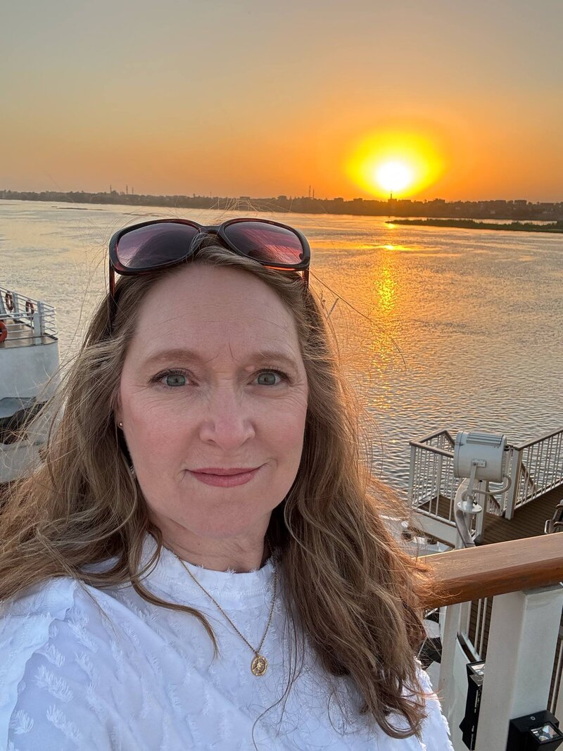 Terra from Adventures by Terra standing on the top deck of AmaLilia river cruise ship on the Nile River with the sun setting in the background