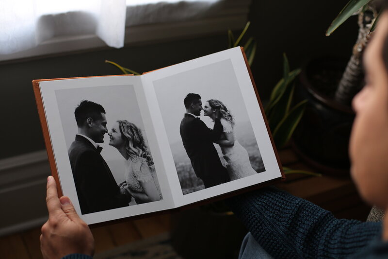 Man holding  open wedding album showing two black and white pictures of a couple on their wedding day- Romero Album Design
