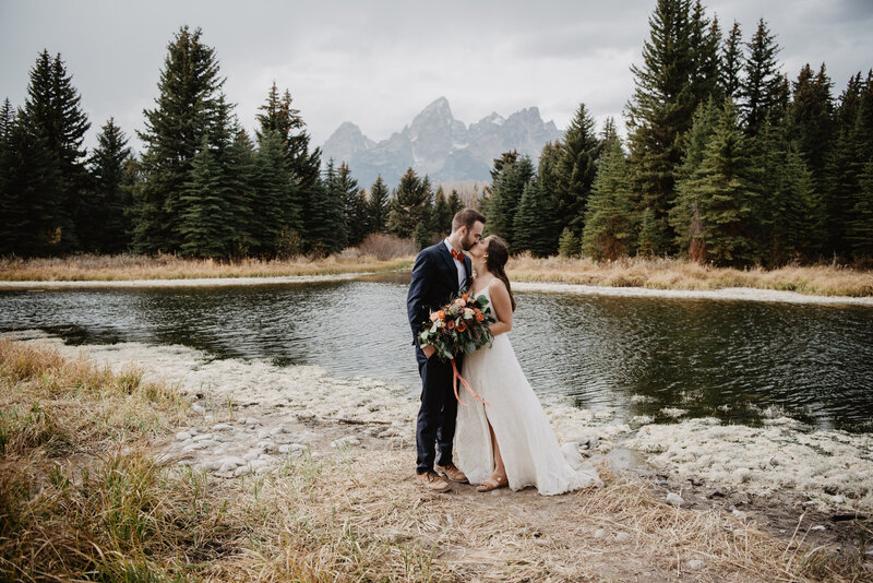 autumn wedding in the grand tetons with bride and groom kissing on the shore of a pond at schwabacher landing for their jackson hole wedding