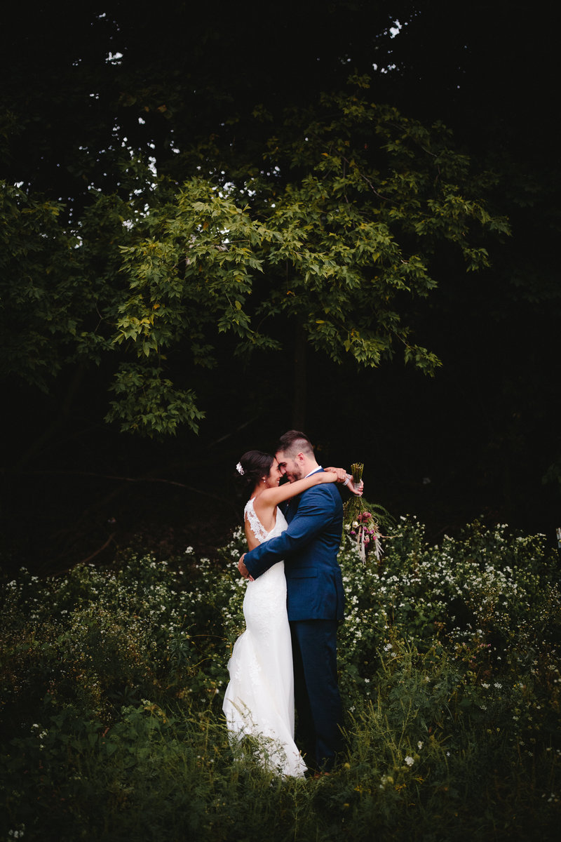 Bride wrapping her arms around her groom in a field.