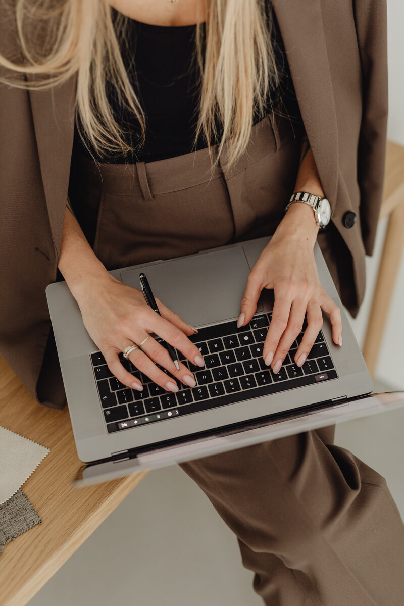 young woman entrepreneur dressed in brown suit types on laptop