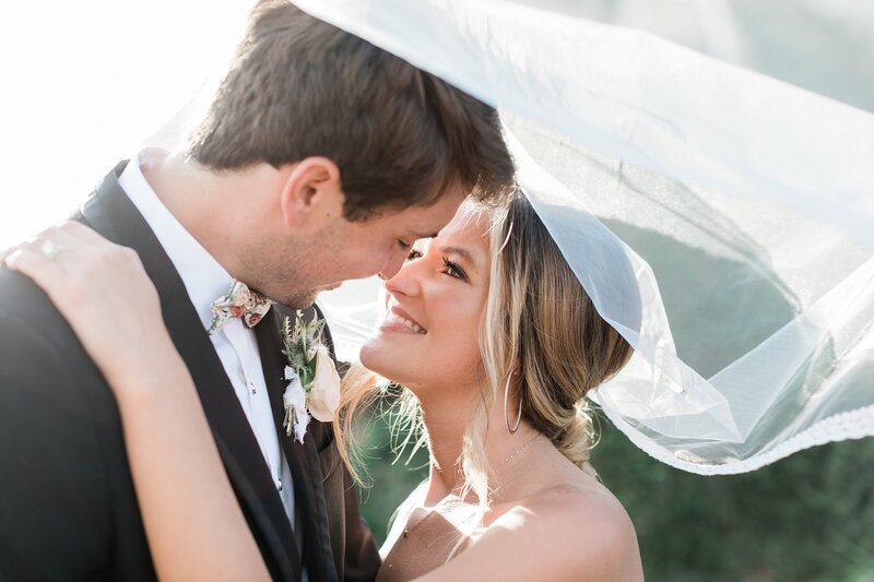 Bride and groom smiling with their heads close together under the veil during their wedding day portraits at Olde Dobbin Station