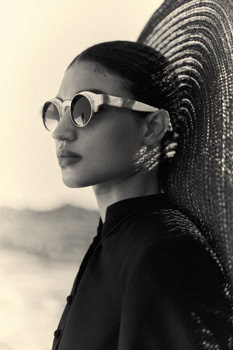 Black and white photo of a model wearing stylish sunglasses and looking off into the distance.