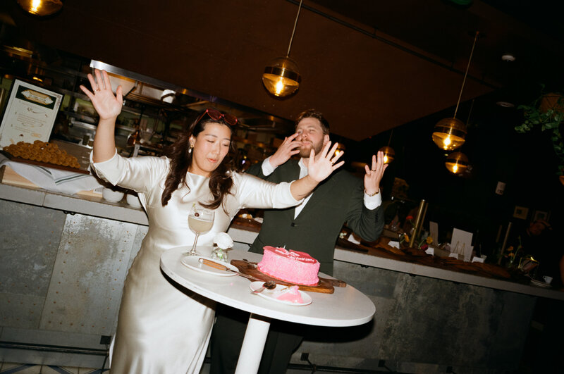 Film photo of a couple at their wedding reception at Terra in Boston, celebrating in front of a bright pink cake with expressive joy — photographed by a film wedding photographer.