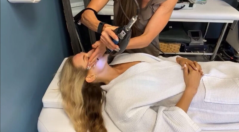 A woman receiving a facial cryotherapy treatment from a professional in a treatment room, showcasing the therapeutic services offered at 212 Salon, Spa, & Barbershop.