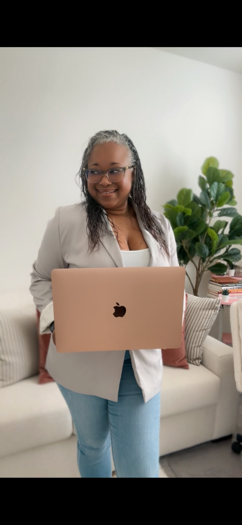 Letitia Hopkins smiling in her office wearing jeans, a white tank top, and blazer, holding her laptop and looking to the side, embodying self-love, casual confidence, and Main Character Energy as a life, love, and relationship coach empowering women to create aligned, fulfilled lives and relationships.