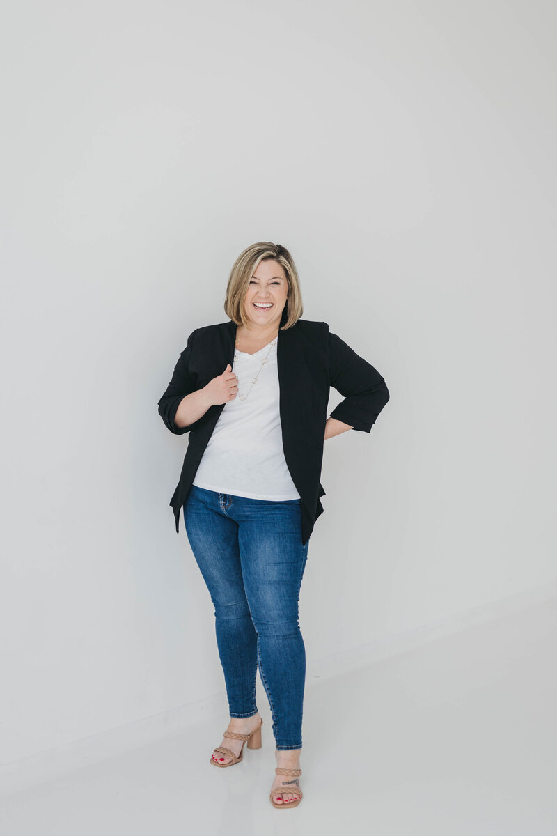 woman in jeans and a black blazer in front of a blank white wall