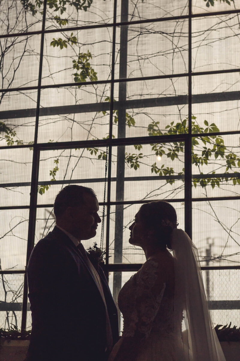 Latino couple gazing into each others eyes in a  conservatory like venue Viridian Images photo wedding planner Tinted Events Design and Planning
