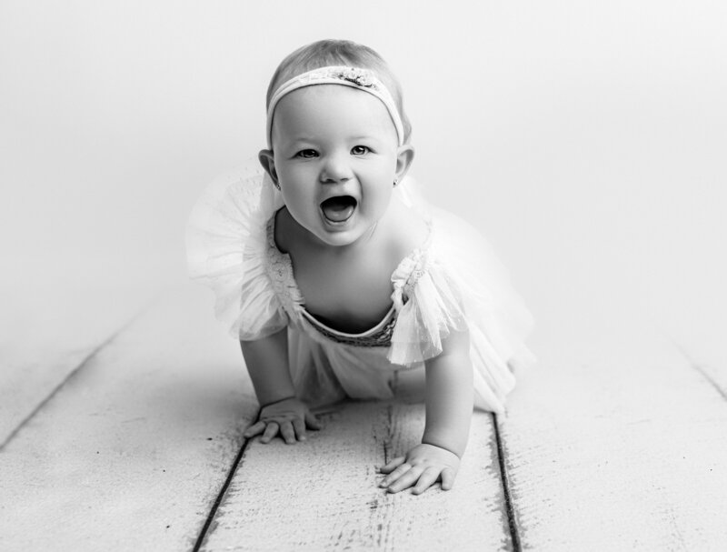 Black and white portrait of one year old girl crawling and smiling at cmaera