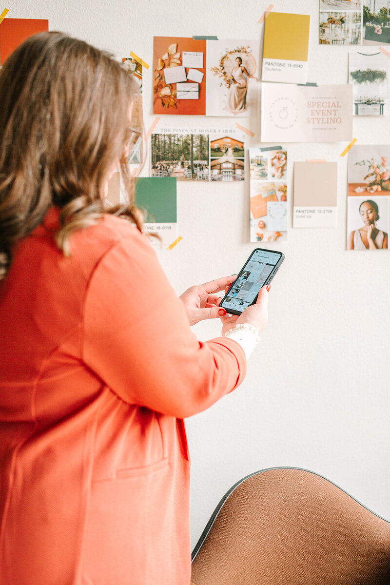 Katelynn looking at a phone in front of a branding brainstorm wall