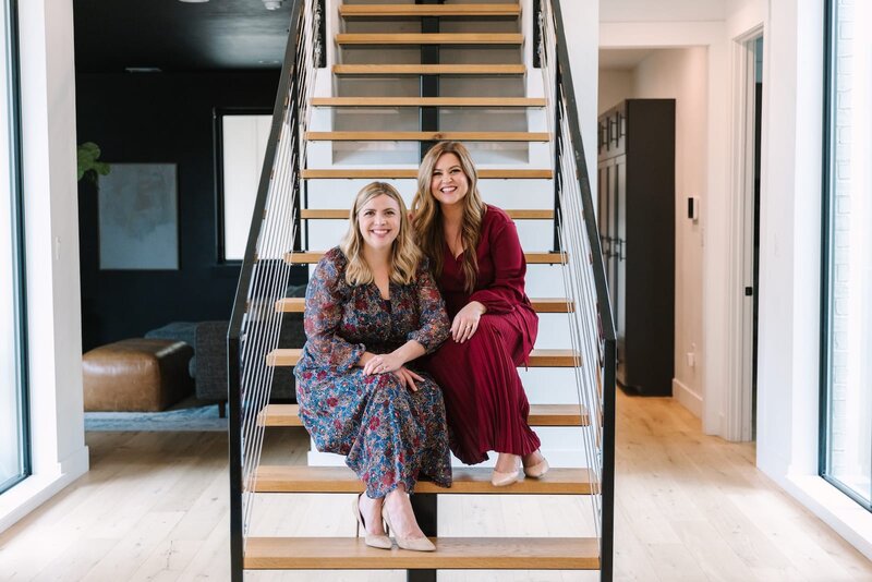 Dallas real estate experts Keelie and Brianna of Haven Realty Group sitting together on stylish staircase in a contemporary home.
