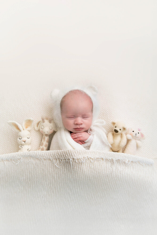 newborn baby girl wrapped in white with a white bear hat laying on a white background for her newborn photography session in Hamilton, Ontario.